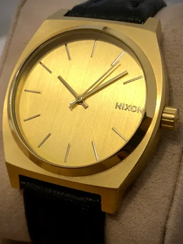 The Time Teller standing upright on a watch cushion, its brushed gold dial, line indices and Nixon logo at 3 o'clock